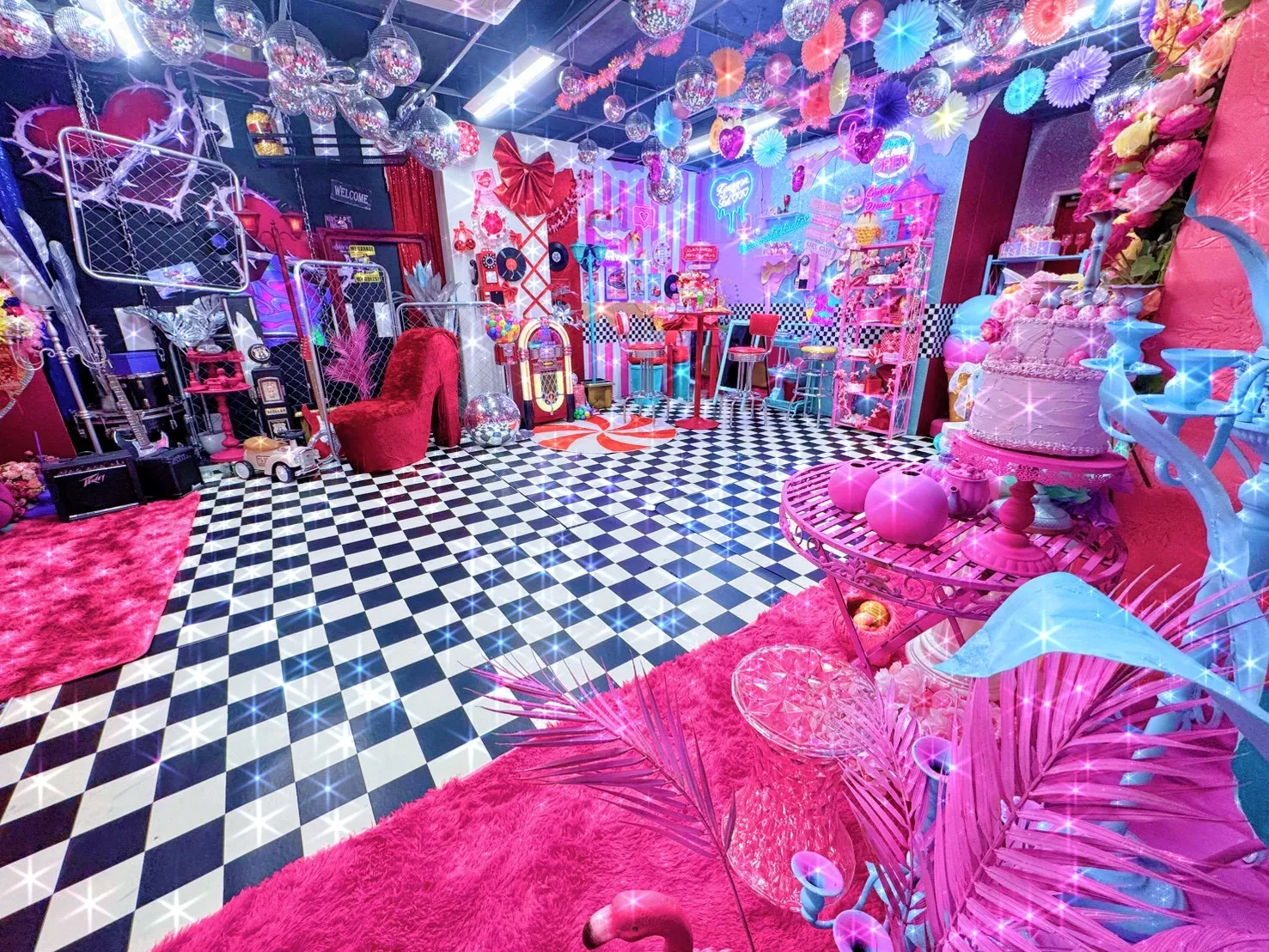 白黒チェックの床にピンクのファーラグを敷いたダイナー風撮影スペースの全景。ハイヒール型ソファやケーキのオブジェ、ミラーボールが彩る