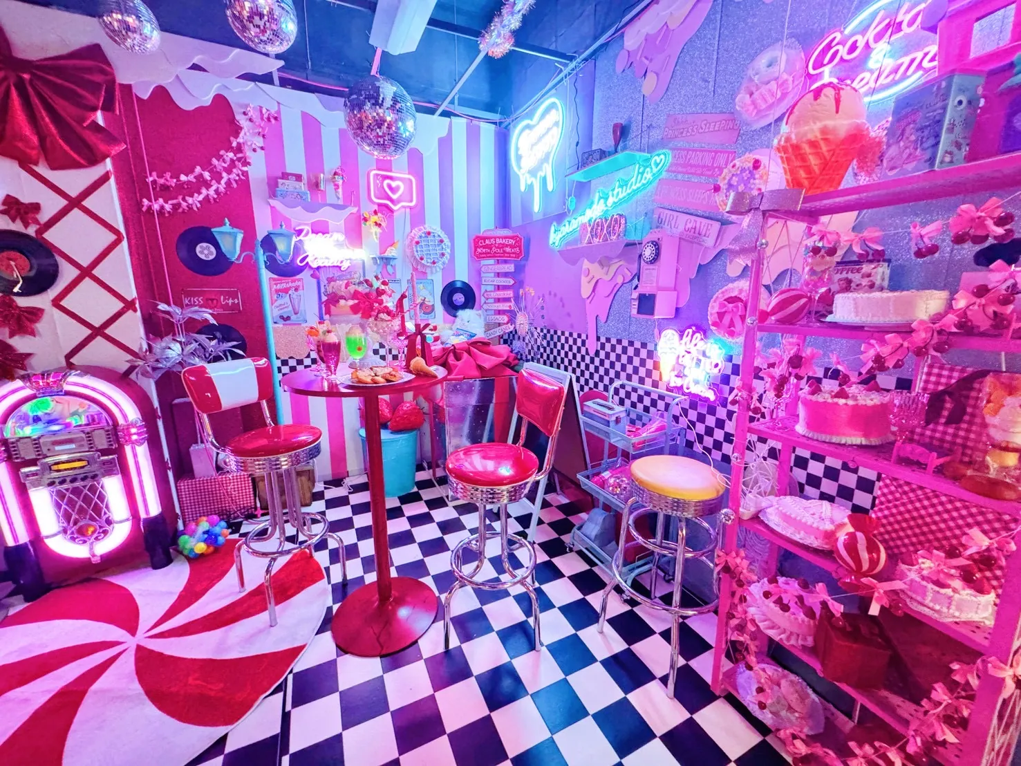 赤いダイナーチェアとピンクのハイテーブルにクリームソーダやスイーツを並べたポップな撮影スペース。白黒チェッカー床とネオンが夜のダイナー気分を演出