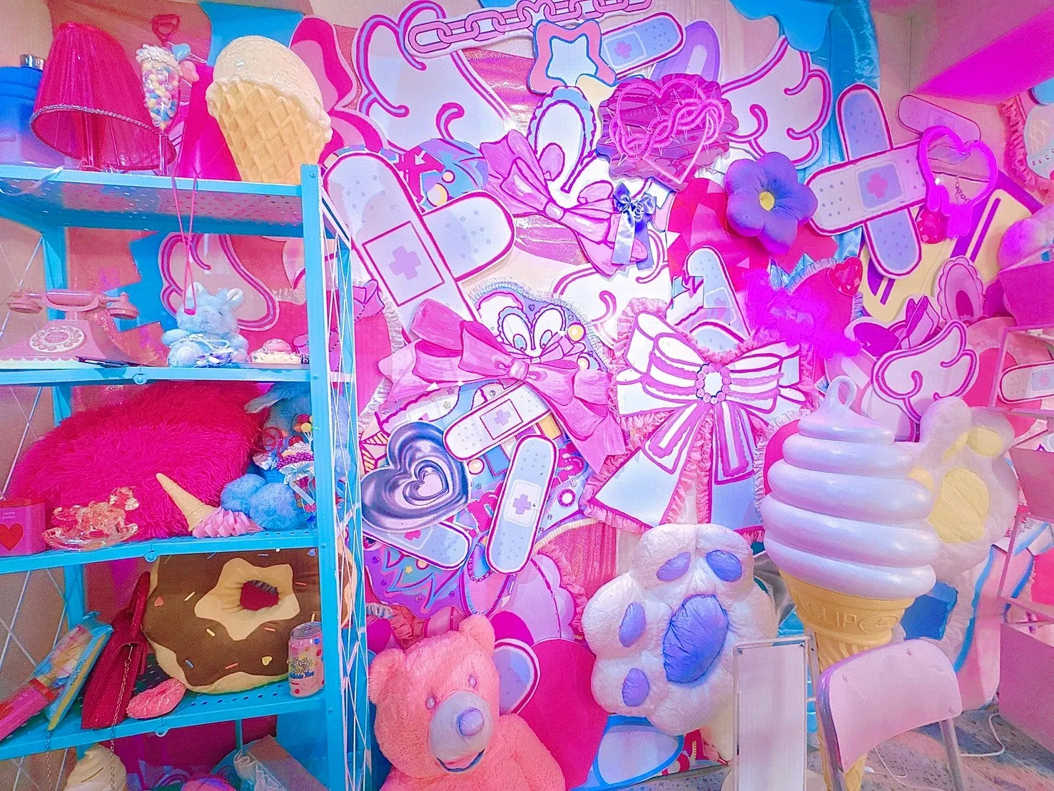絆創膏やリボンのポップなアートで彩られた壁が目を引く撮影ブース。水色の棚にドーナツクッションやぬいぐるみ、巨大なソフトクリームのオブジェも並ぶ